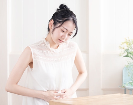 お腹を押さえ辛そうにする女性、生理痛など女性特有の不調を表現
